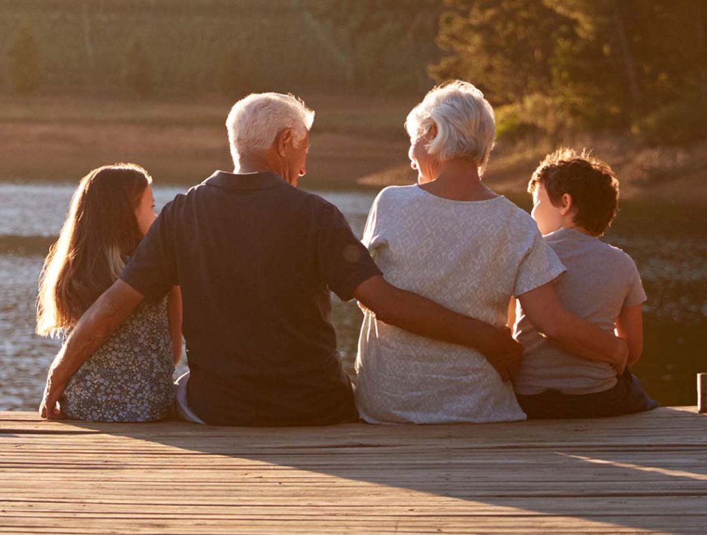 Grandparents and their grandchildren overlook a lake from a dock.