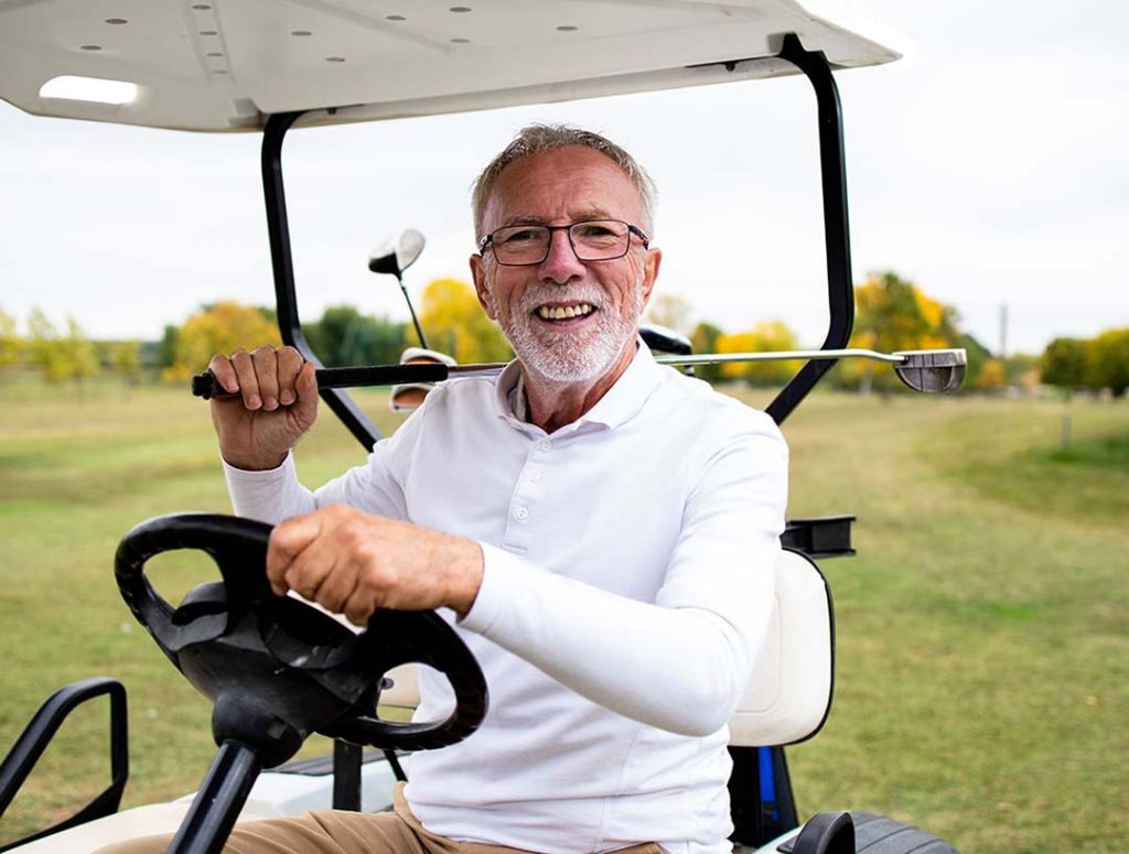 Man smiles while driving golf cart with golf club in hand.