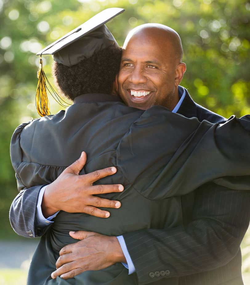 Father hugs his son at his graduation with a smile on his face.