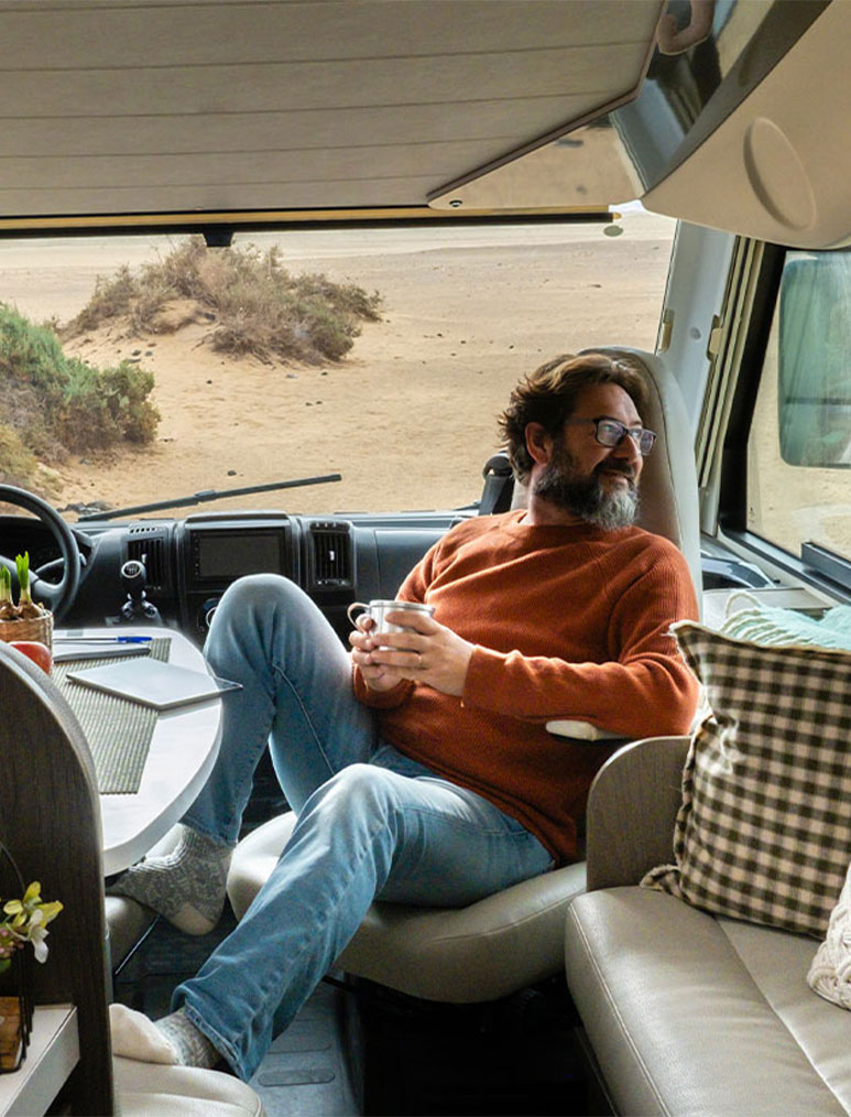 Man enjoys the view from his RV while drinking a cup of coffee.
